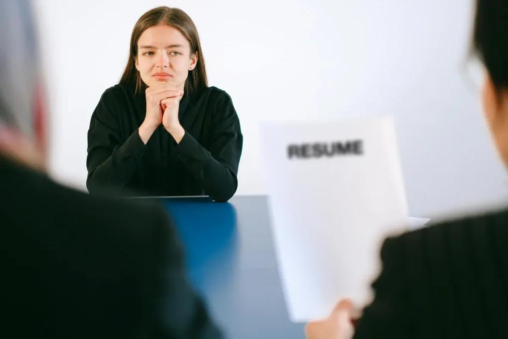 Seorang wanita dalam wawancara kerja dengan dua pewawancara yang fokus pada resume di meja