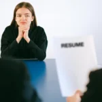 Seorang wanita dalam wawancara kerja dengan dua pewawancara yang fokus pada resume di meja
